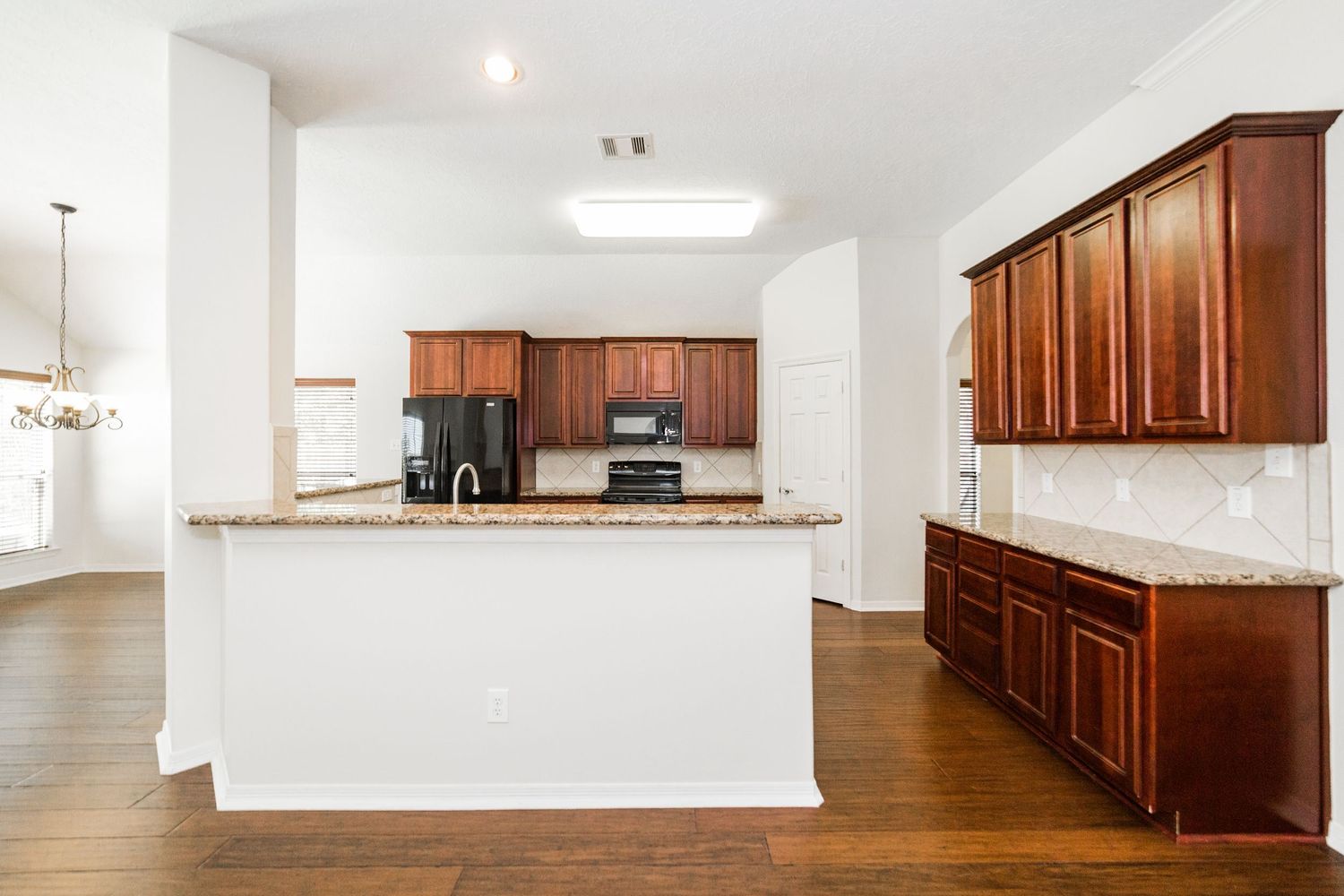Open kitchen with cherry wood cabinets, granite counters, and black appliances.