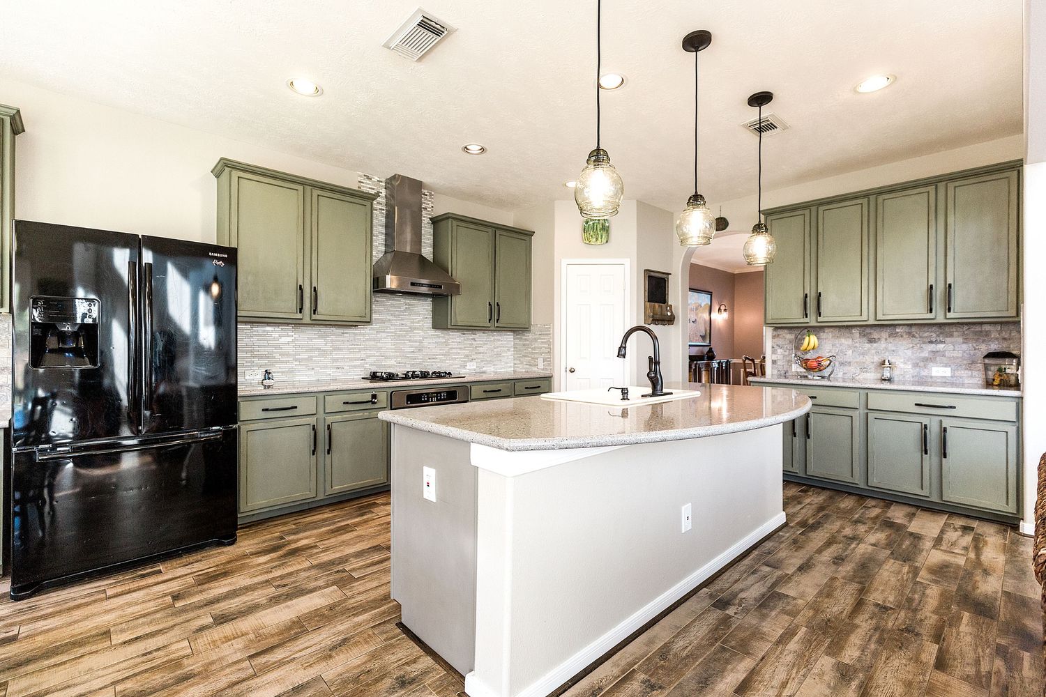 Contemporary kitchen with sage green cabinets, white island, wood floors, and black fridge.