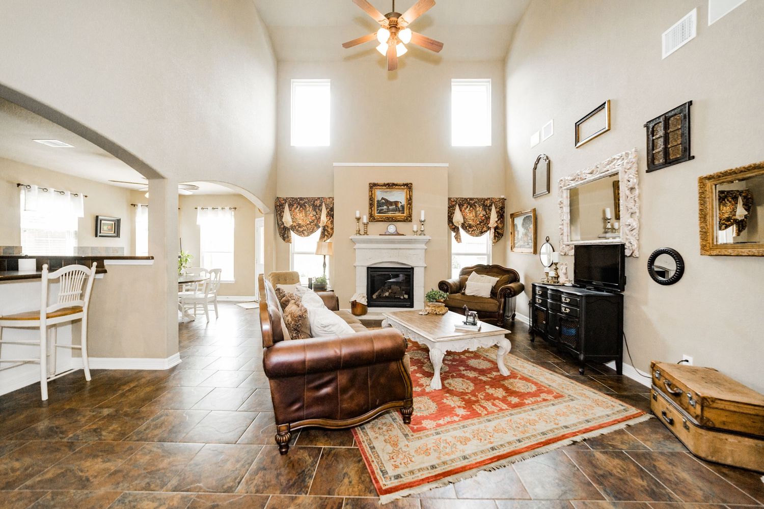 Spacious living room with high ceilings, fireplace, leather furniture, and dark tile floors.