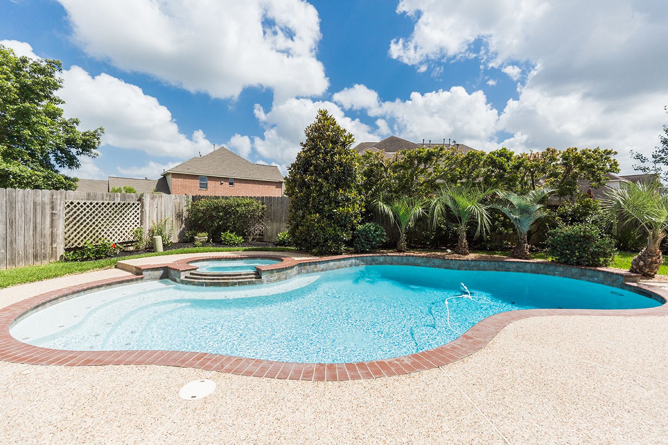 Backyard oasis featuring a freeform swimming pool with spa, brick coping, lush landscaping, and wood privacy fence.