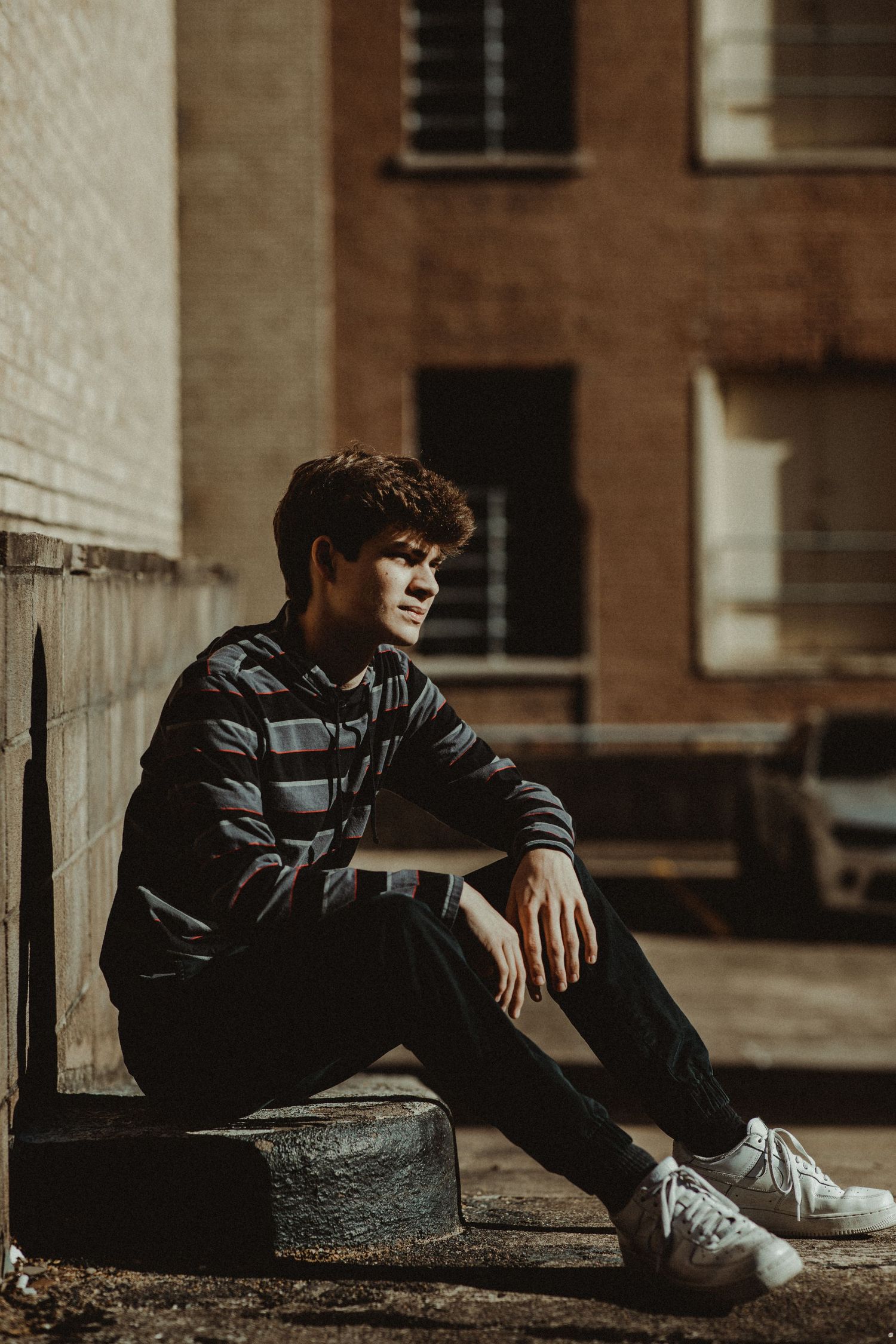 Young man in striped shirt sitting on steps in urban setting outdoors.