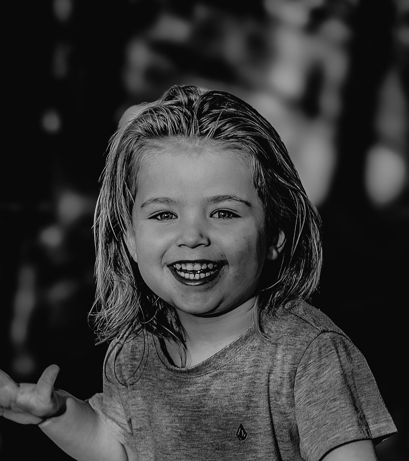 Black and white close-up portrait of laughing young child in gray tee with bokeh background.