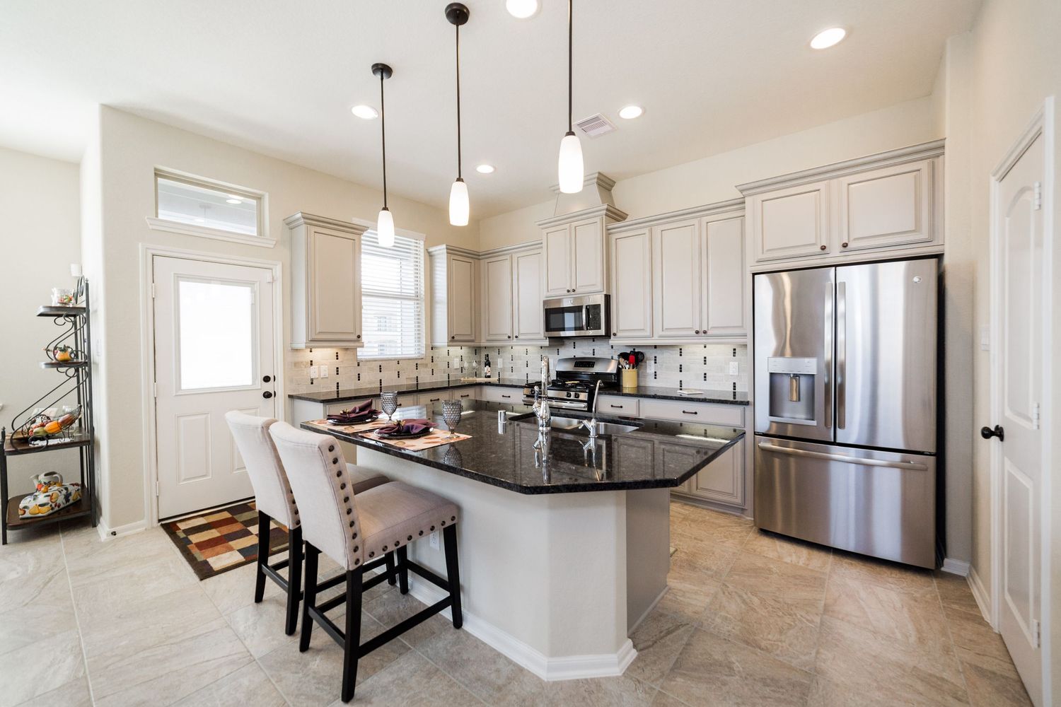 Modern white kitchen with island, pendant lights, dark granite counters, and stainless appliances.