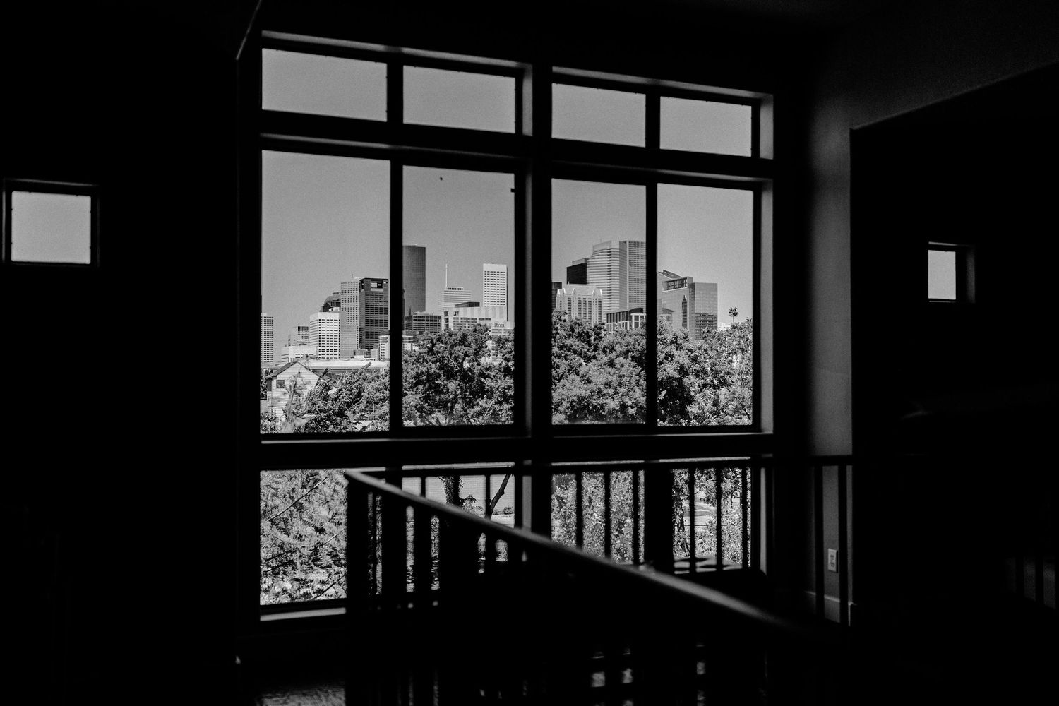 Black and white photo of city skyline viewed through large windows from a dark interior stairwell.