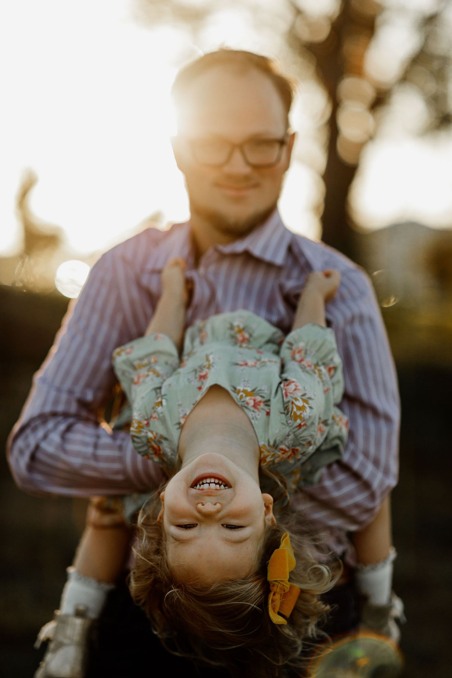 Father holding laughing child upside down in golden sunset light outdoors.