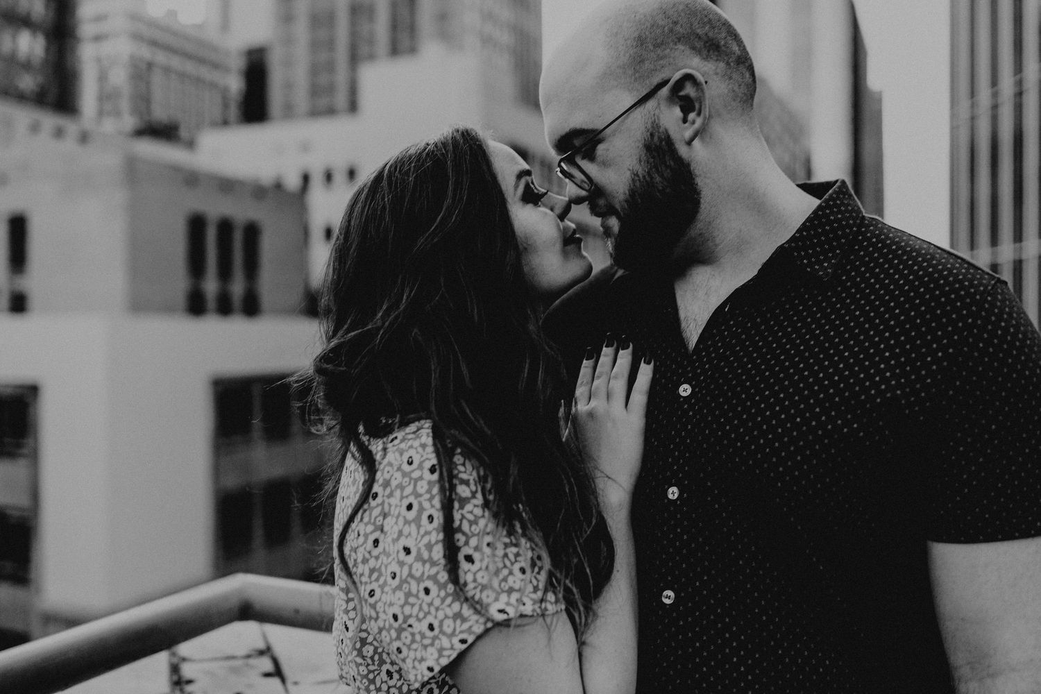 Black and white photo of couple sharing a kiss on city rooftop.