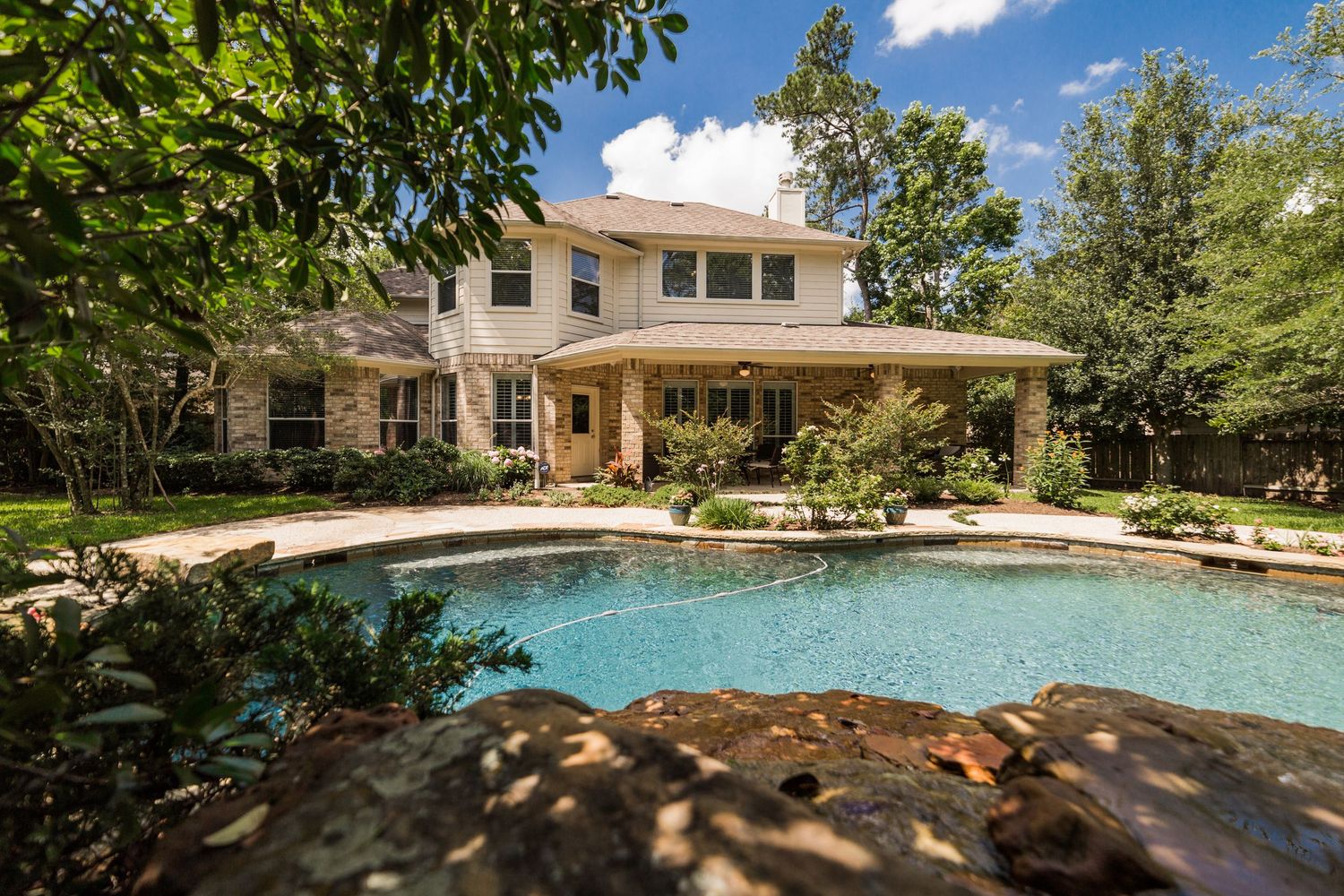 Elegant two-story brick home with a freeform swimming pool surrounded by lush mature trees in a private backyard.