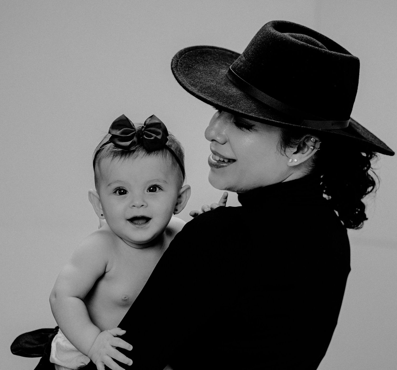 Black and white portrait of a mother in a wide-brim hat holding her baby.