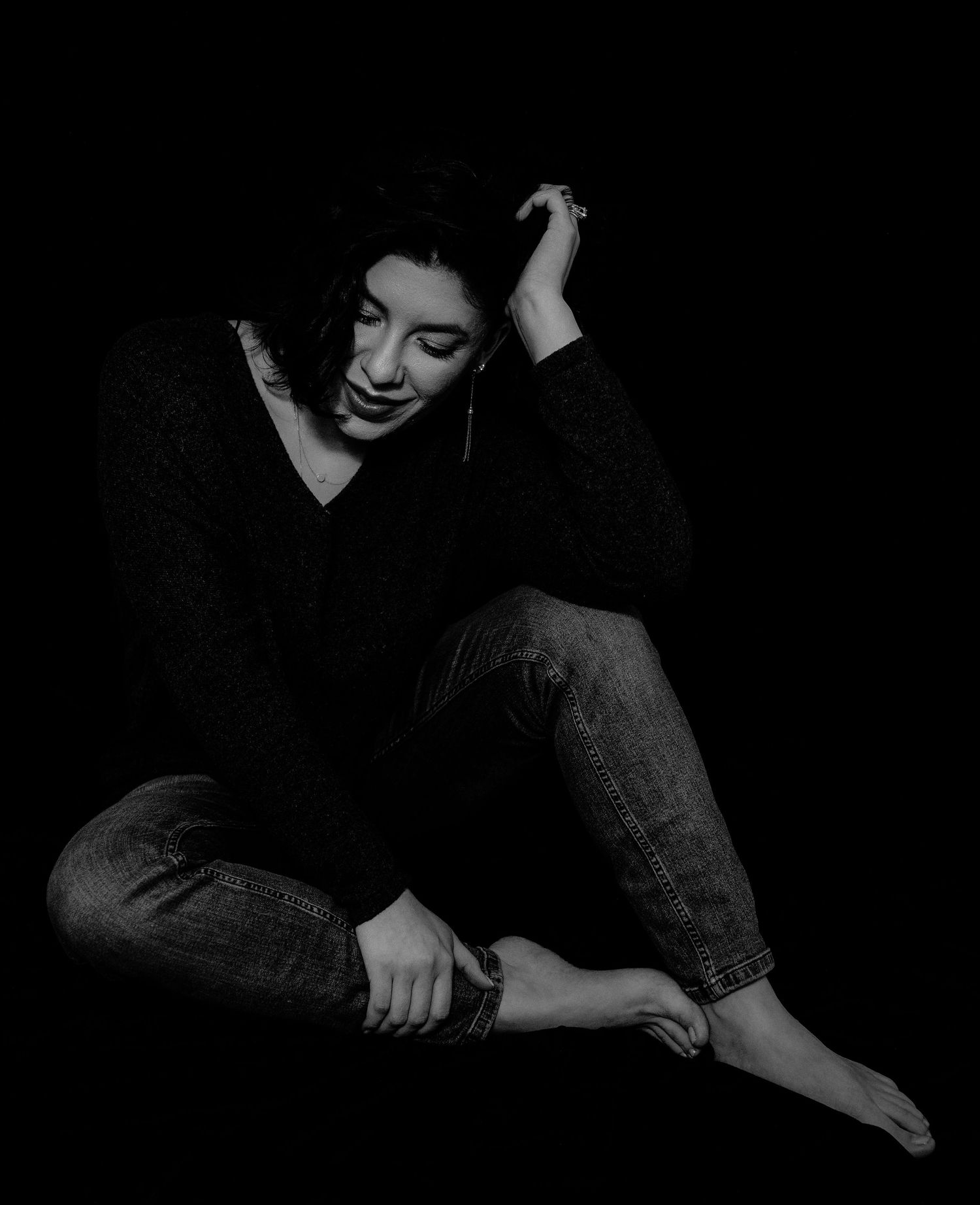 Black and white portrait of smiling woman sitting on floor in casual outfit.