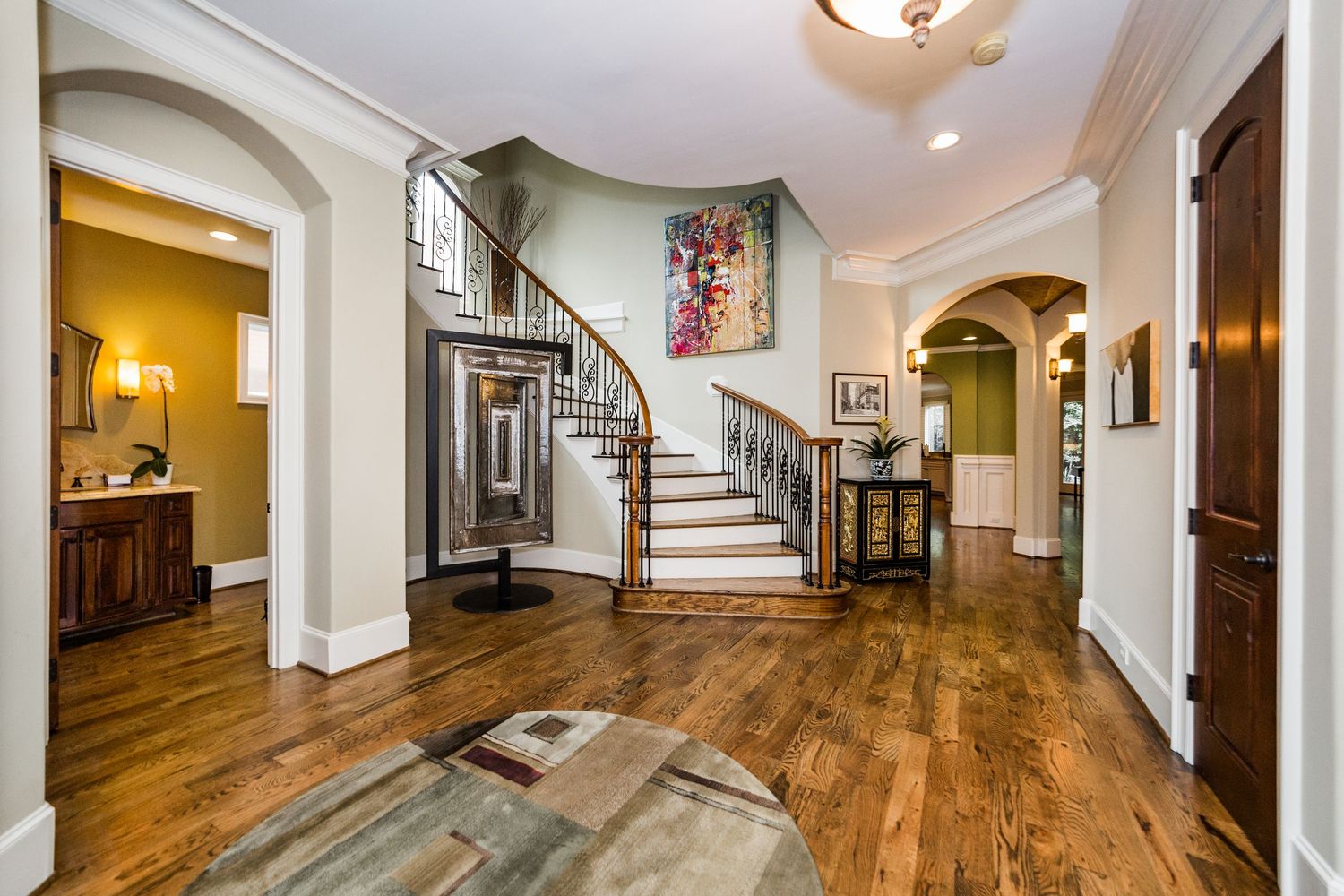 Elegant foyer with curved staircase, hardwood floors, arched doorways, and crown molding in a luxury home.