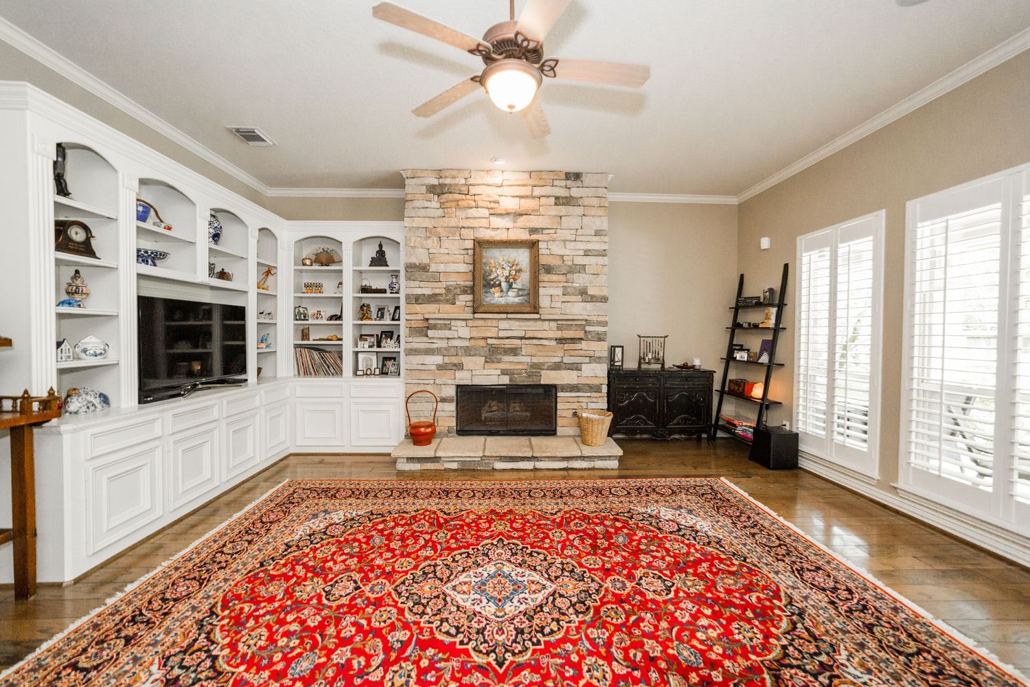 Elegant living room featuring a stone fireplace, built-in white shelving, hardwood floors, and a vibrant red Persian rug.