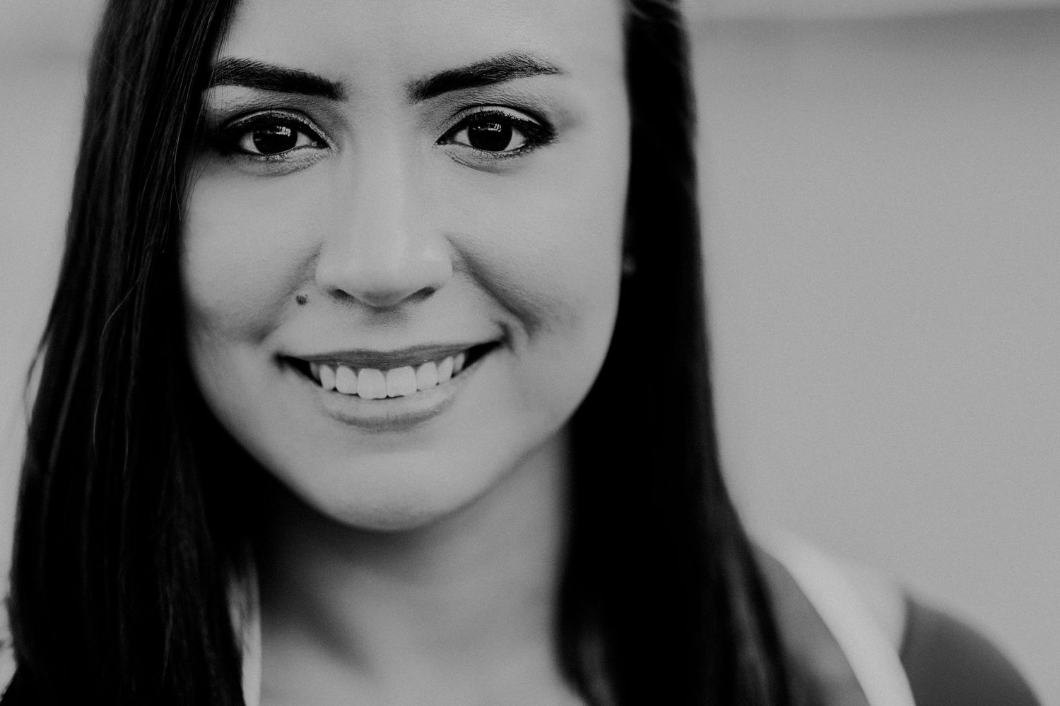 Black and white portrait of a smiling young woman with long dark hair and a nose piercing.