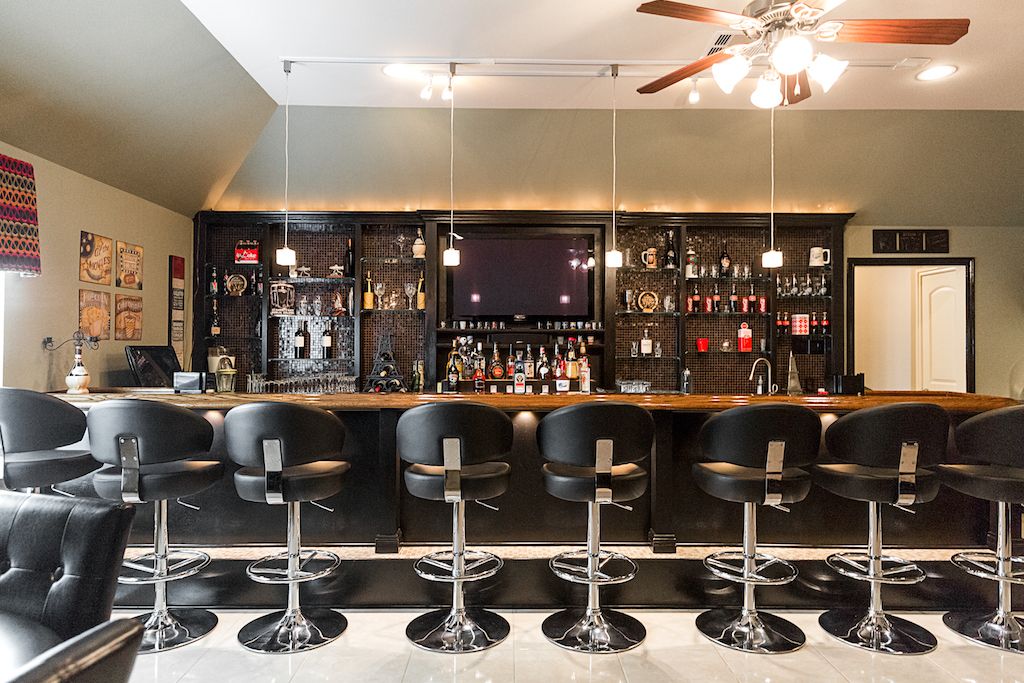 Elegant home bar with black leather stools, chrome bases, and a fully stocked back bar with pendant lighting.