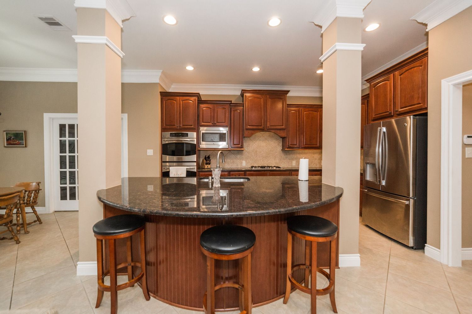 Elegant kitchen with dark cherry cabinets, curved island with bar seating, and stainless appliances.
