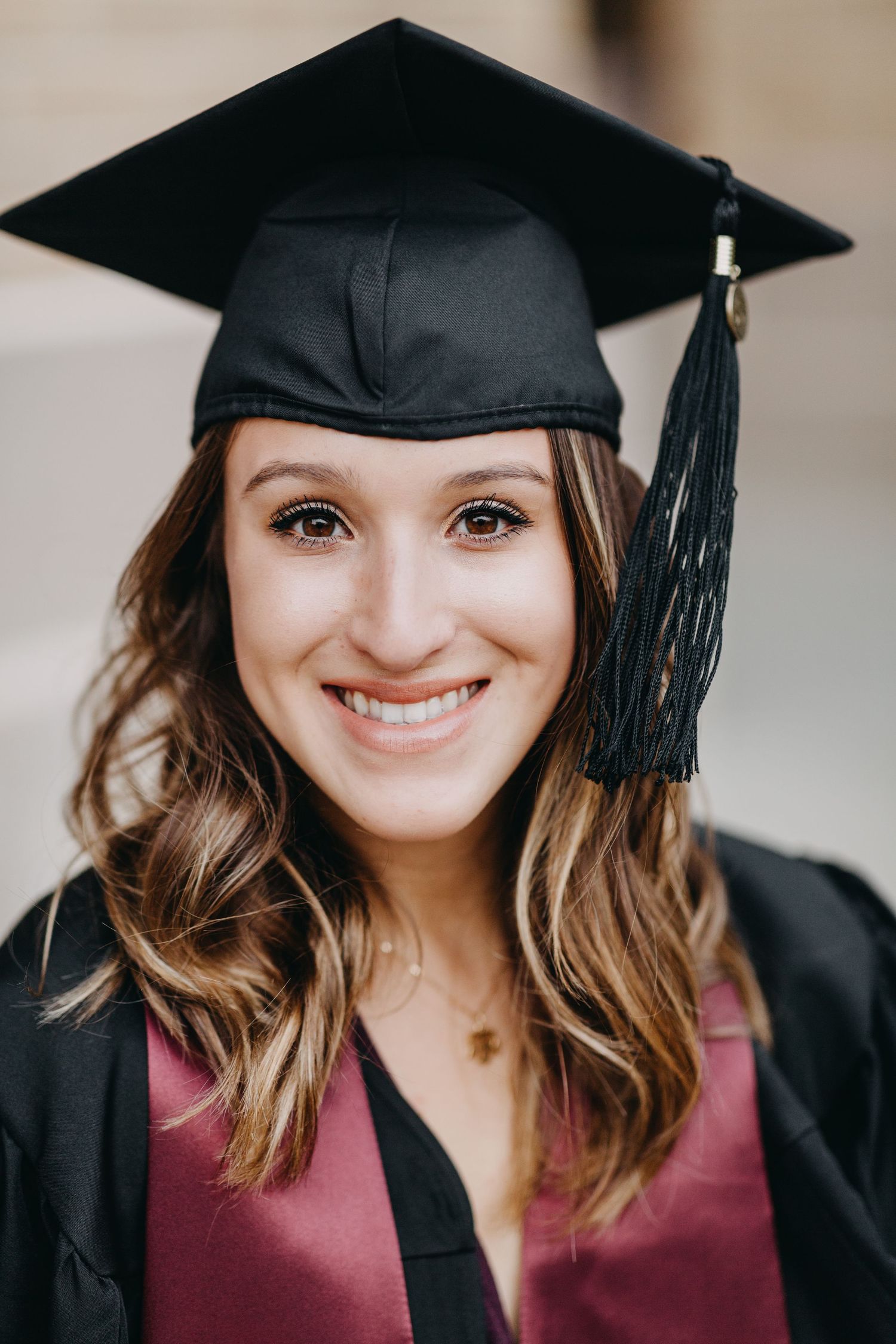 Smiling young woman wearing a black graduation cap and burgundy gown, celebrating her academic achievement.