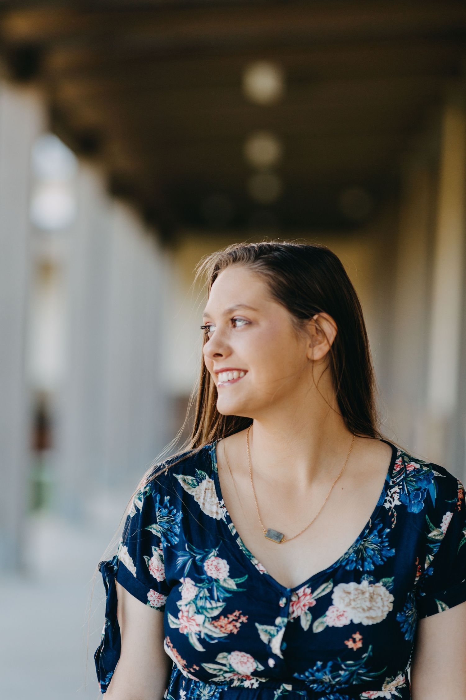 Young woman in floral navy dress smiling outdoors in a covered walkway, portrait photography.
