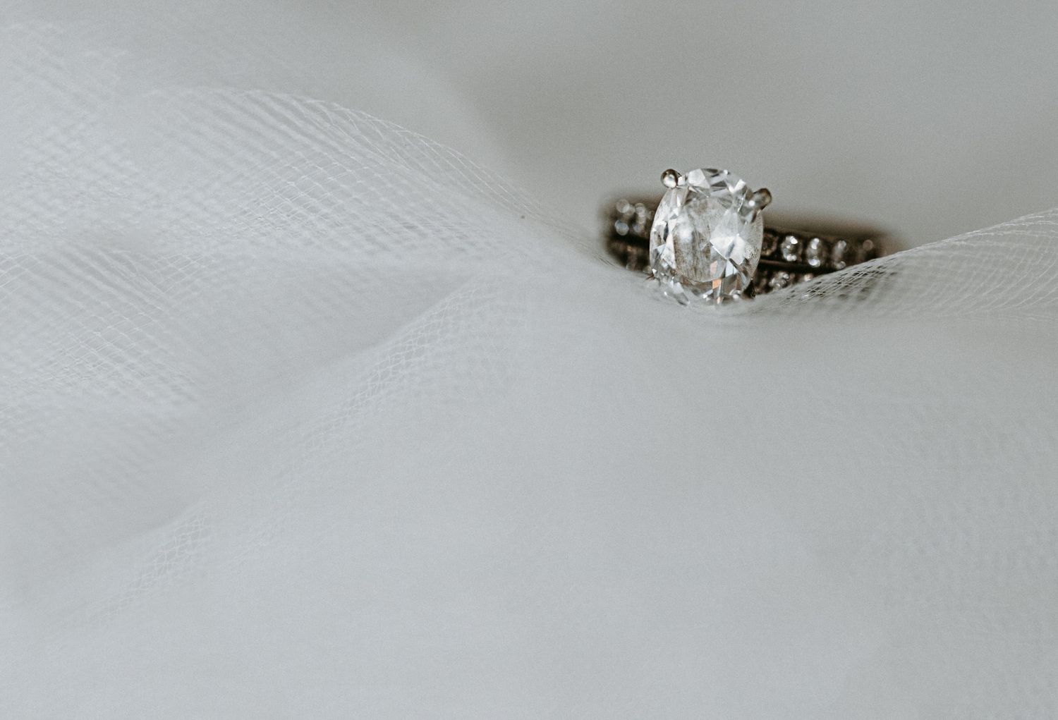 Oval diamond solitaire engagement ring resting on white bridal veil.