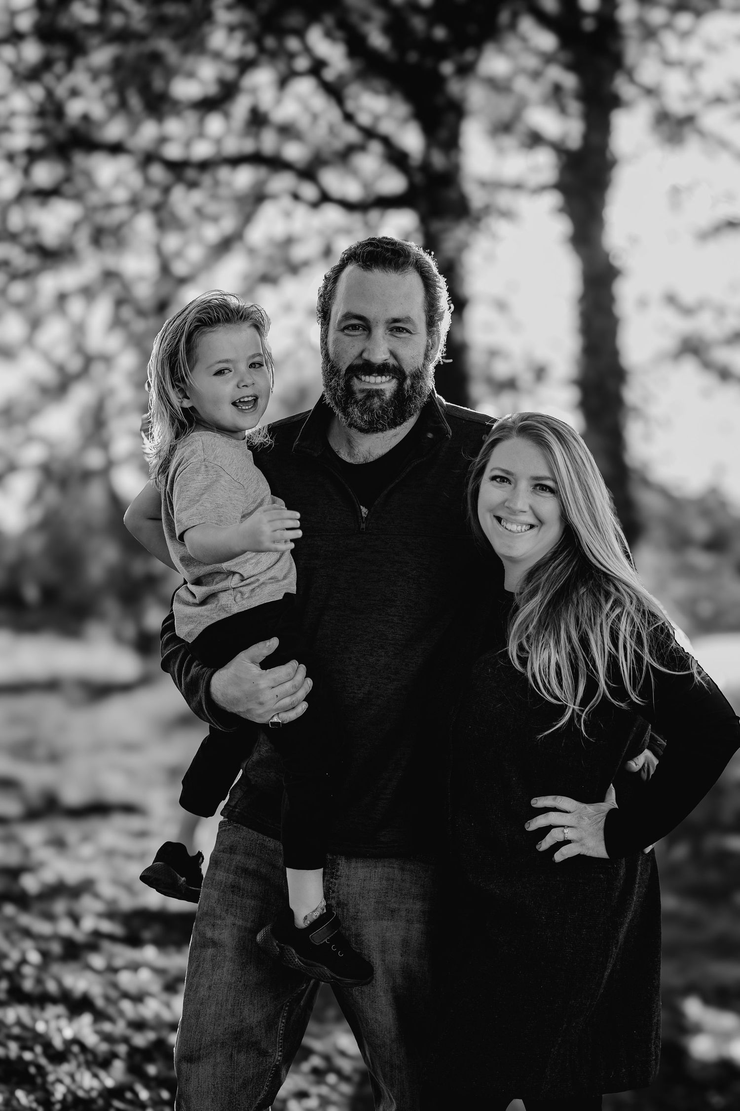 Happy family of three posing together in black and white outdoor portrait photo.