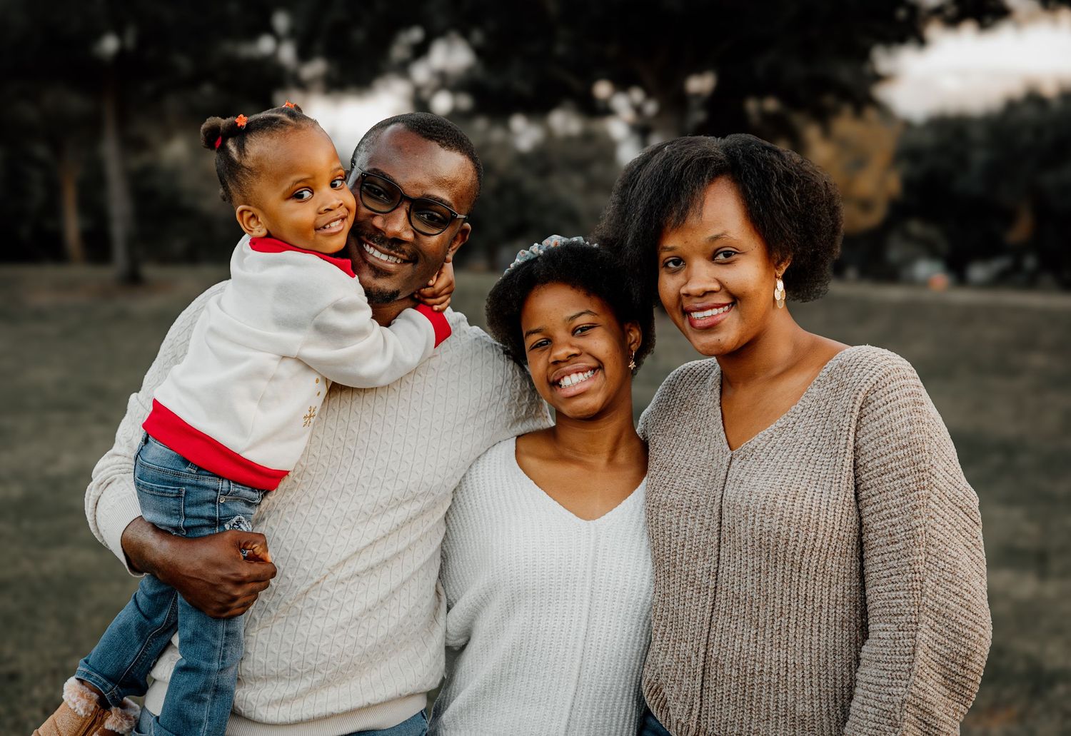Happy Black family of four smiling outdoors in a park during golden hour.