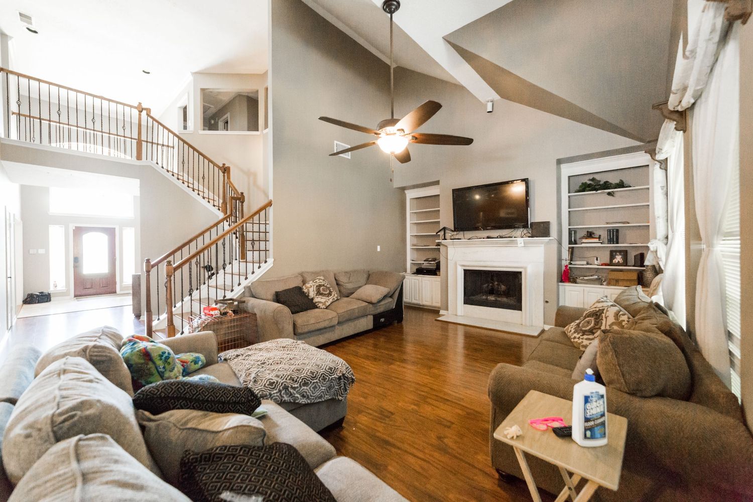 Spacious open-concept living room with vaulted ceilings, hardwood floors, ceiling fan, fireplace, and elegant staircase.