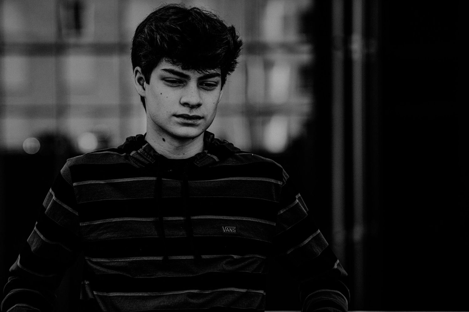 Black and white portrait of a young man in a striped hoodie looking down thoughtfully.
