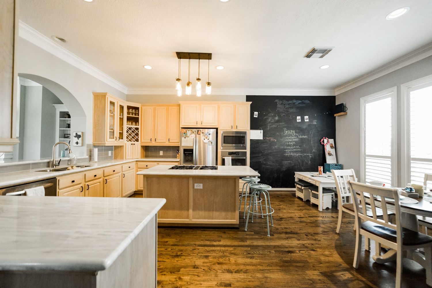 Modern open-concept kitchen with light wood cabinets, chalkboard accent wall, island seating, and hardwood floors.