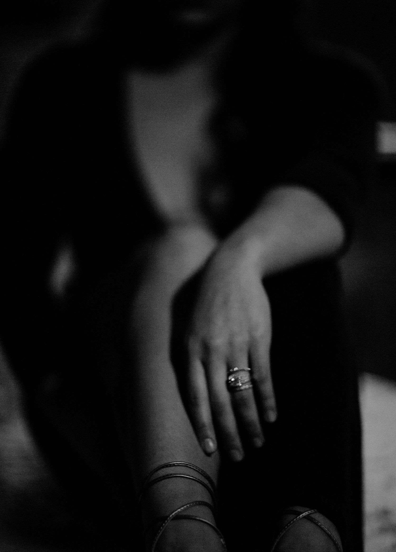Black and white photo of a woman sitting with a diamond ring and bracelet on her hand resting on her knee.