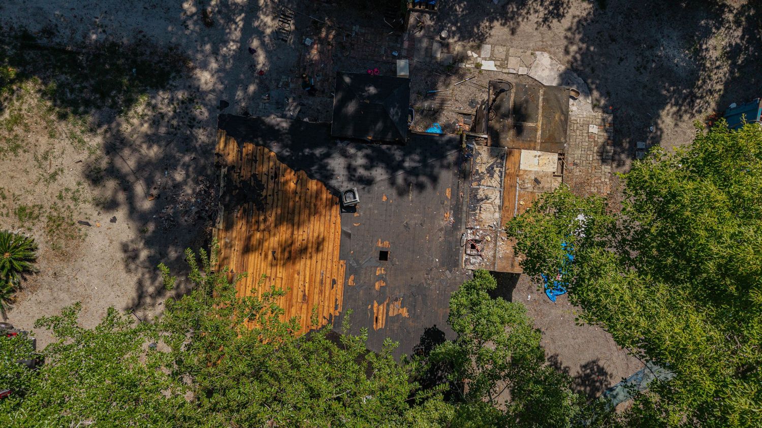 Aerial view of a wooden deck surrounded by lush green trees casting shadows on the ground below.