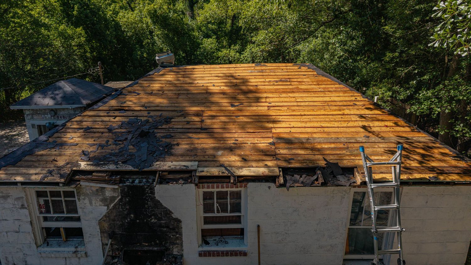 Aerial view of a house undergoing roof renovation with exposed wooden decking and a ladder leaning against the side.