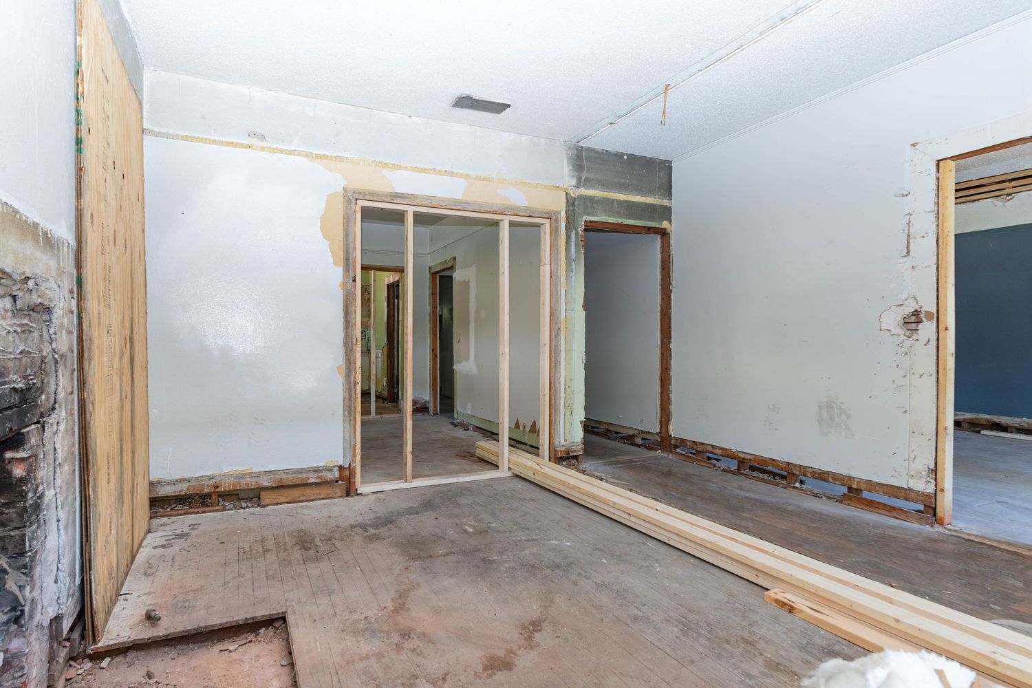 Interior of a home under renovation with exposed wood framing, bare floors, and open doorways in an empty room.