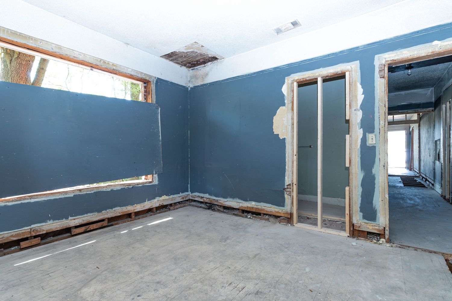 Unfinished room with blue drywall, exposed door frames, and concrete floor in a home under renovation.