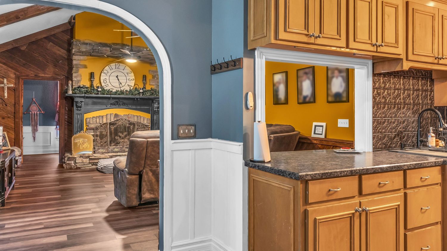 Kitchen with oak cabinets and granite countertops opens to a cozy living room with a fireplace and arched doorway.
