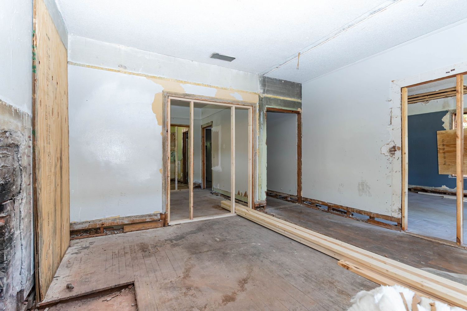 Interior room under renovation with exposed wood framing, drywall, and bare concrete floors in a home remodel.