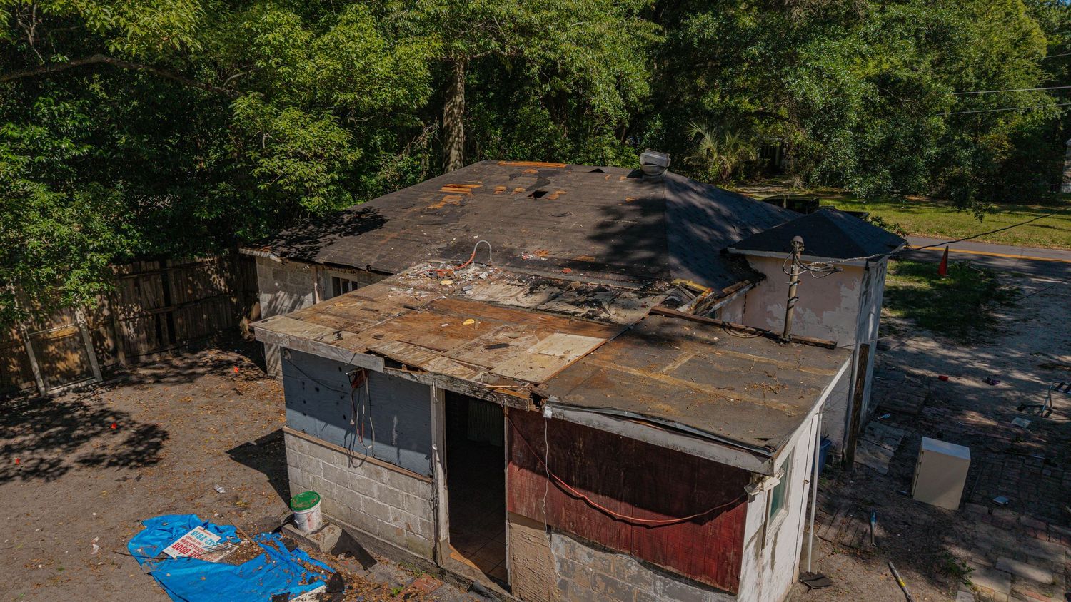 Aerial view of a dilapidated building with damaged roof and rusty metal siding surrounded by trees.