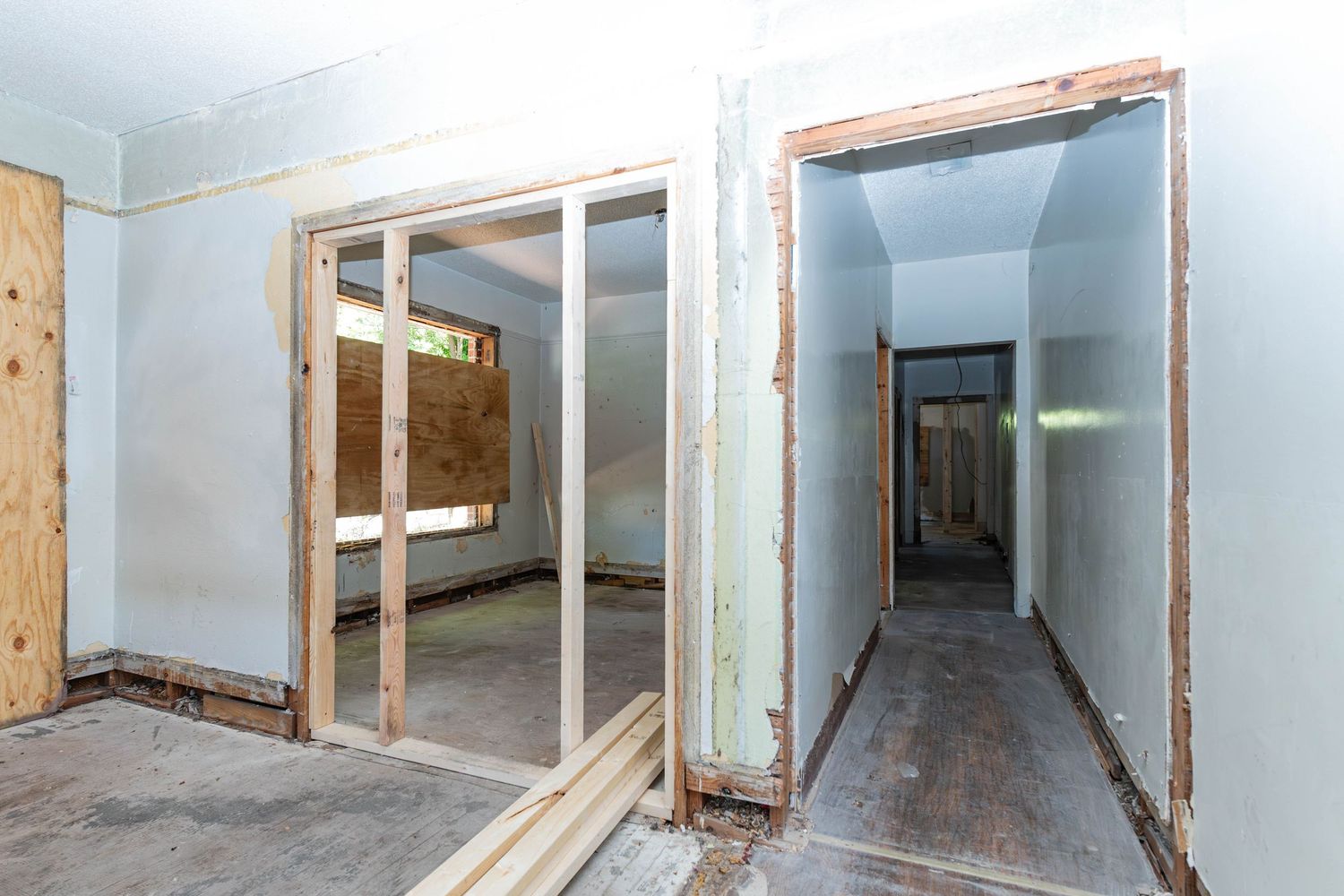 Unfinished home interior showing bare wood door frames, partially demolished walls, and a long hallway during renovation.
