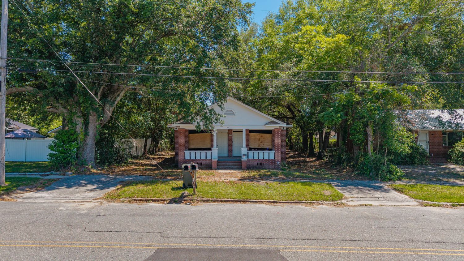 Small bungalow home surrounded by mature trees on a quiet street corner with a covered front porch and brick facade.