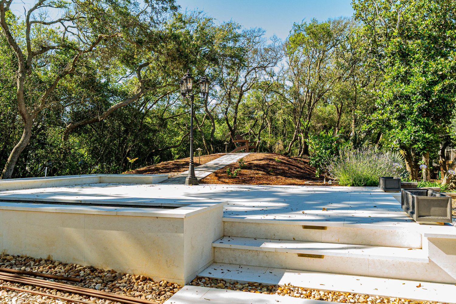 White concrete steps lead to a serene outdoor patio surrounded by lush green trees and landscaped garden paths.