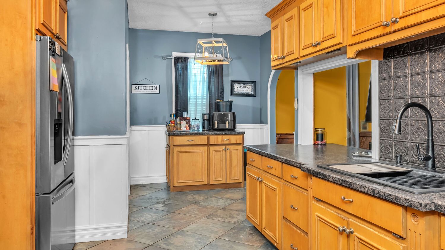 Spacious kitchen with honey oak cabinets, dark granite counters, stainless steel fridge, and blue wainscoting walls.