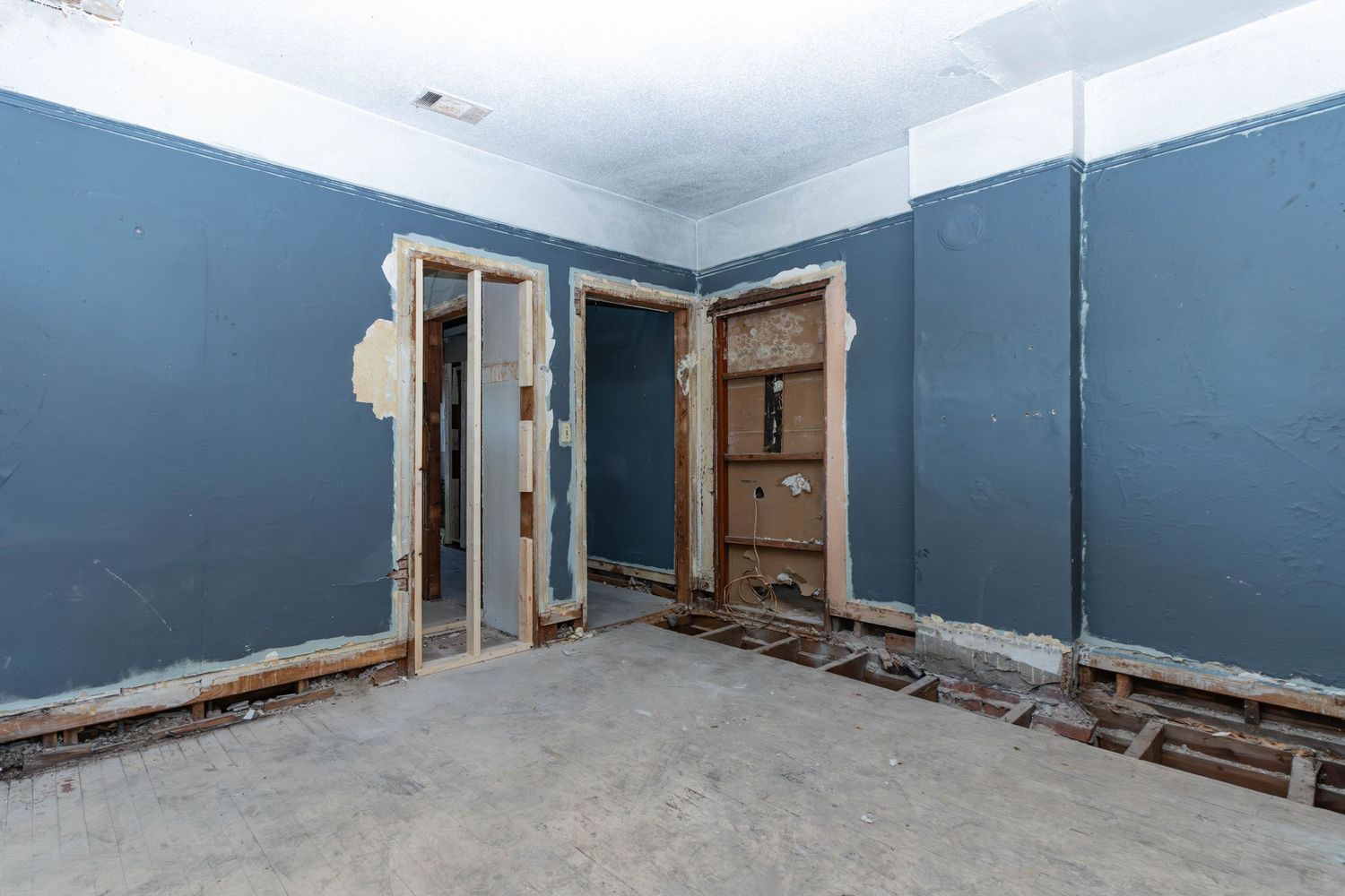 Bare concrete floor room with blue walls, two open doorways, and stripped interior ready for remodeling.