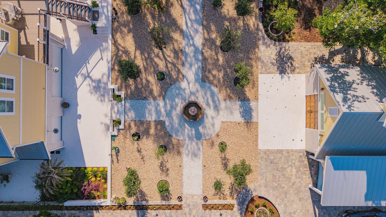 Aerial view of a landscaped courtyard with circular fountain, stone pavers, and lush greenery between buildings.