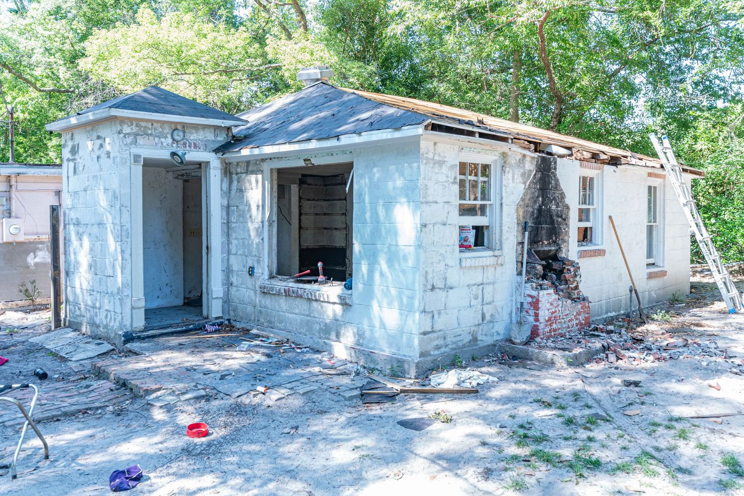 Dilapidated abandoned house with damaged walls, broken windows, and debris scattered around the exterior.
