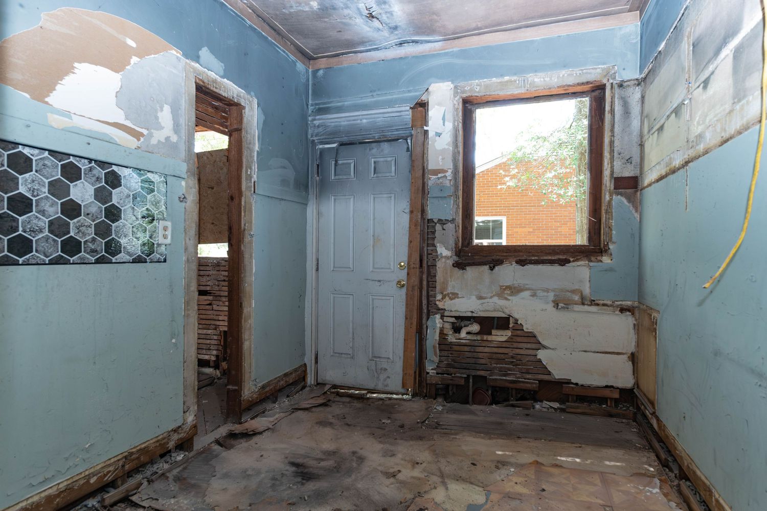 Abandoned room with peeling blue paint, damaged walls, worn tile floor, and two doorways in a dilapidated property.