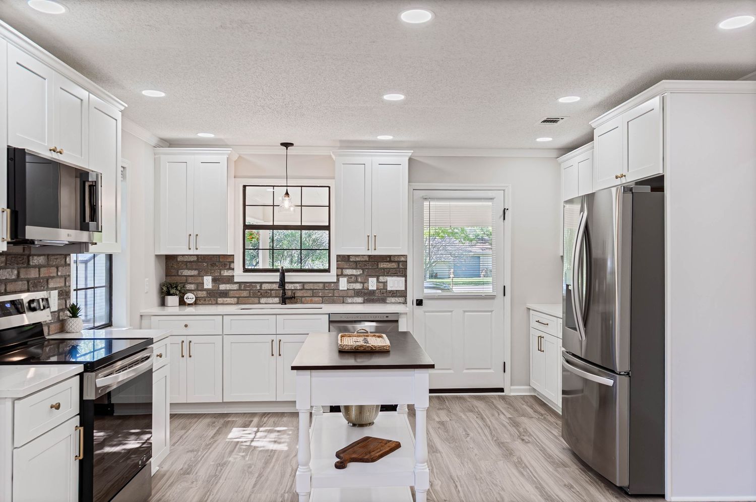 Modern kitchen with white cabinets, stainless steel appliances, brick backsplash, center island, and light hardwood floors.