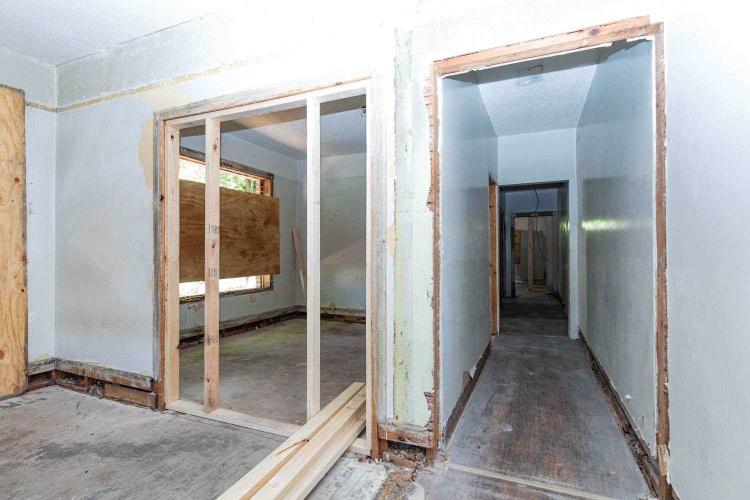 Interior of a home under renovation with exposed wood door frames, drywall, and a hallway visible in the background.