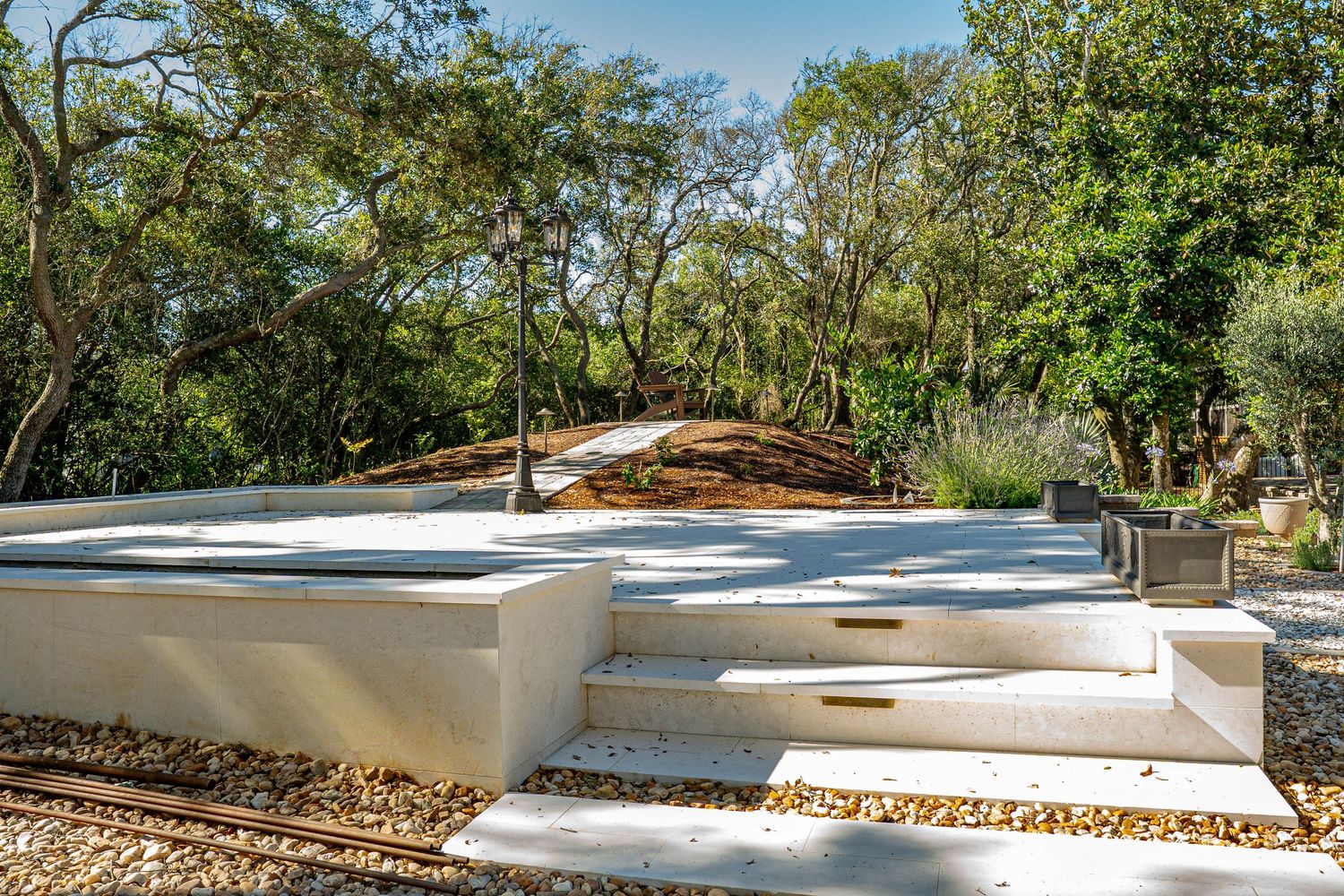 Modern white concrete outdoor steps and platform surrounded by lush green trees and gravel landscaping.