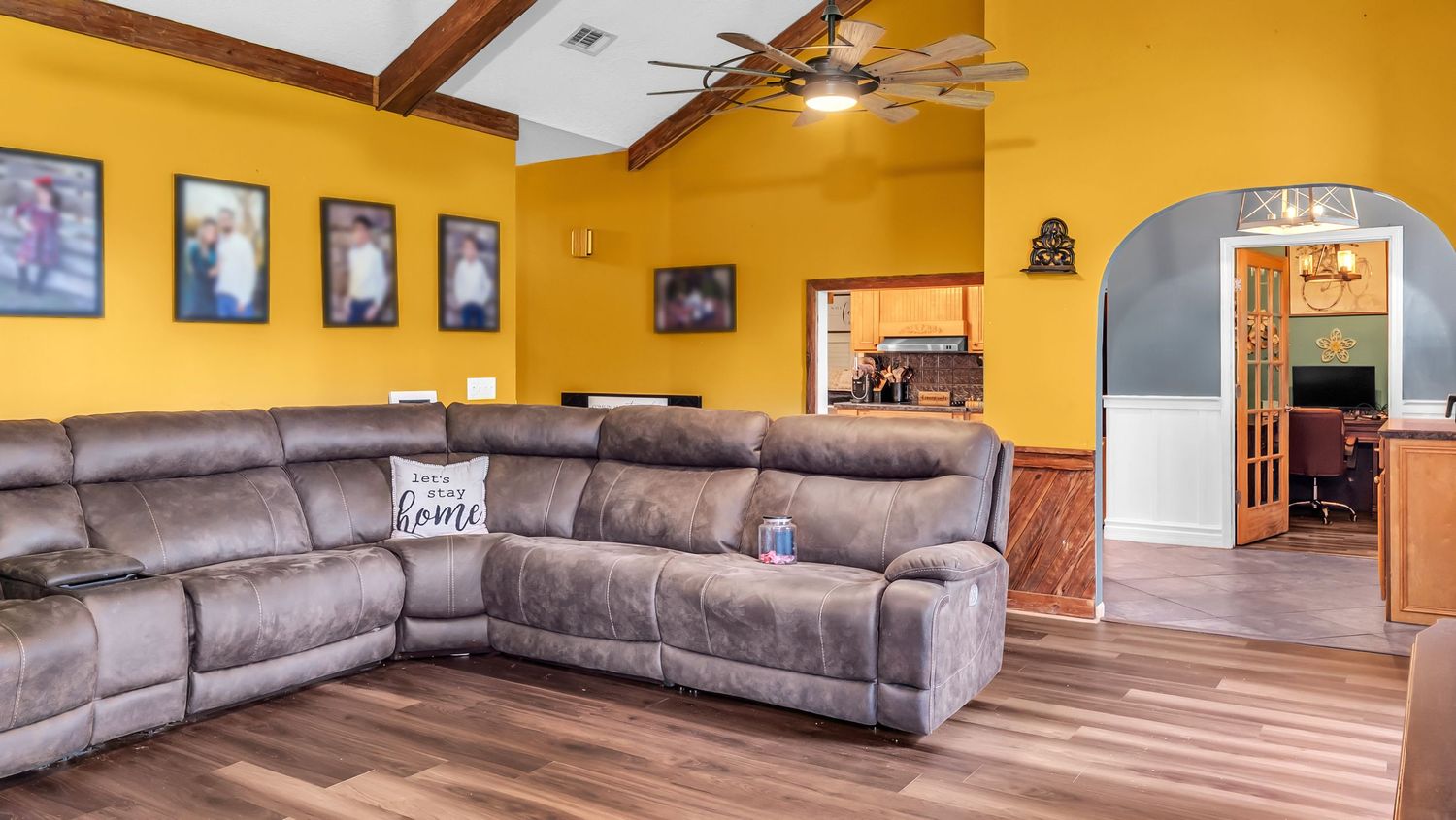 Spacious living room with gray sectional sofa, yellow walls, hardwood floors, ceiling fan, and arched doorway leading to home office.