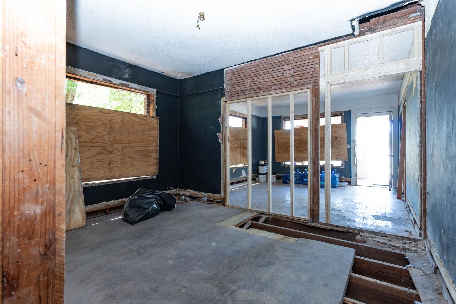 Interior of a home under renovation with exposed walls, plywood, concrete floor, and glass partition framing.