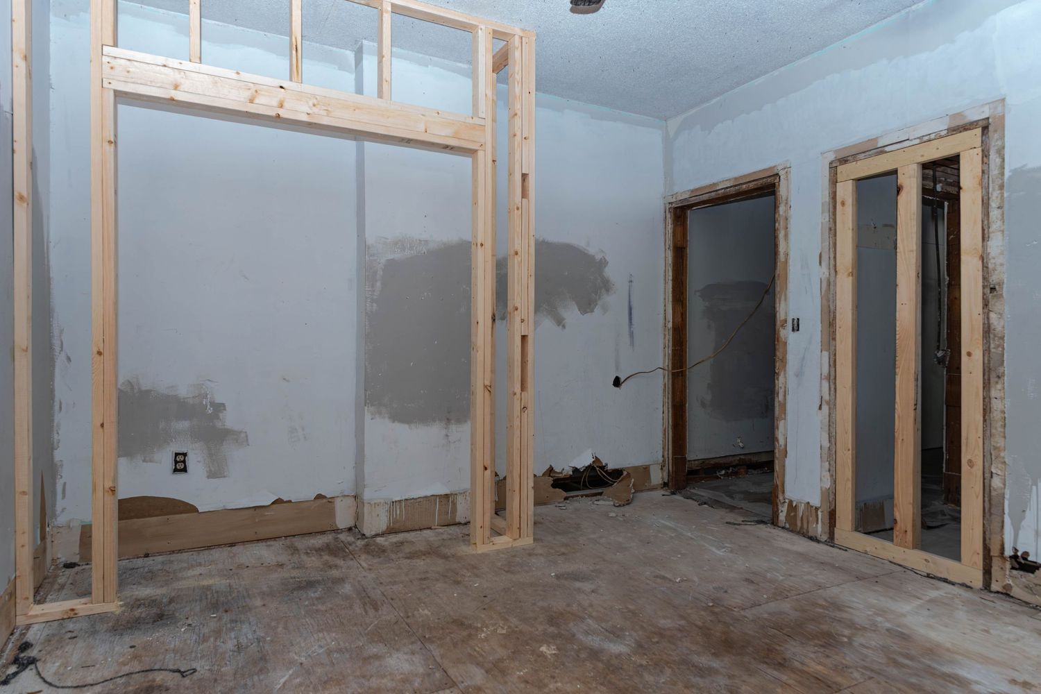Room under renovation with exposed wood framing, drywall patches, and bare floors in a home remodel.