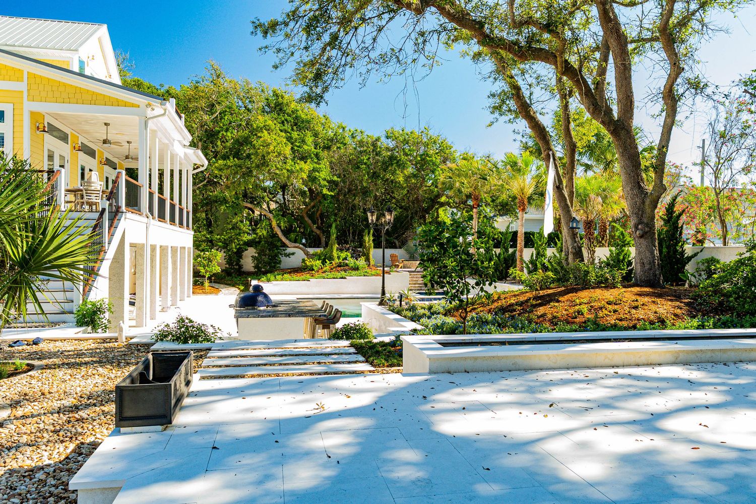 Bright white walkway leads to a yellow cottage surrounded by lush tropical trees and manicured gardens on a sunny day.