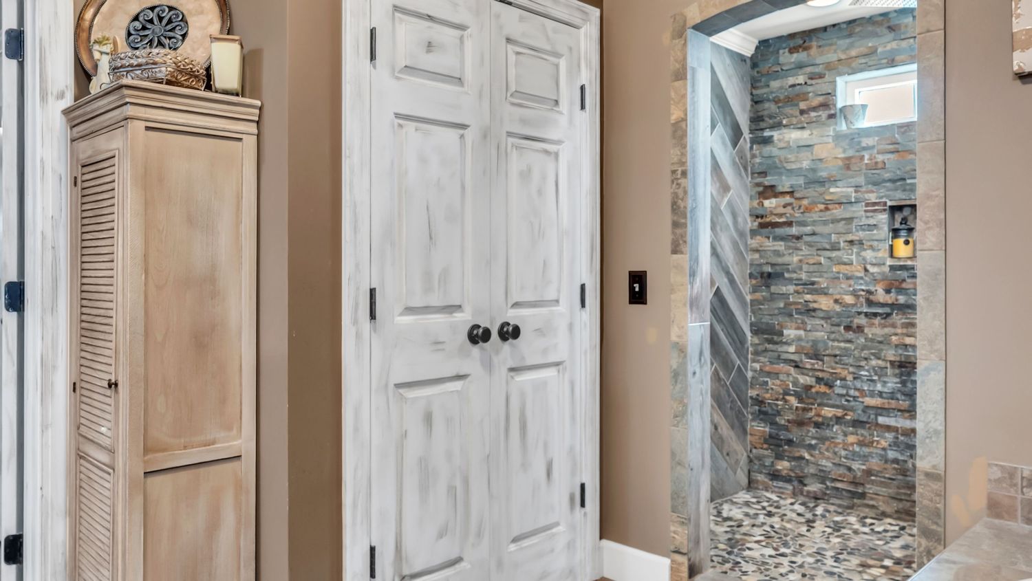 Rustic bathroom featuring whitewashed double doors, wood cabinet, and stone-tiled walk-in shower with pebble floor.